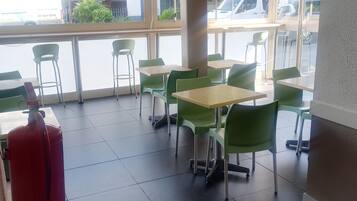 A cafe with tables and chairs, a fire extinguisher, and large windows.