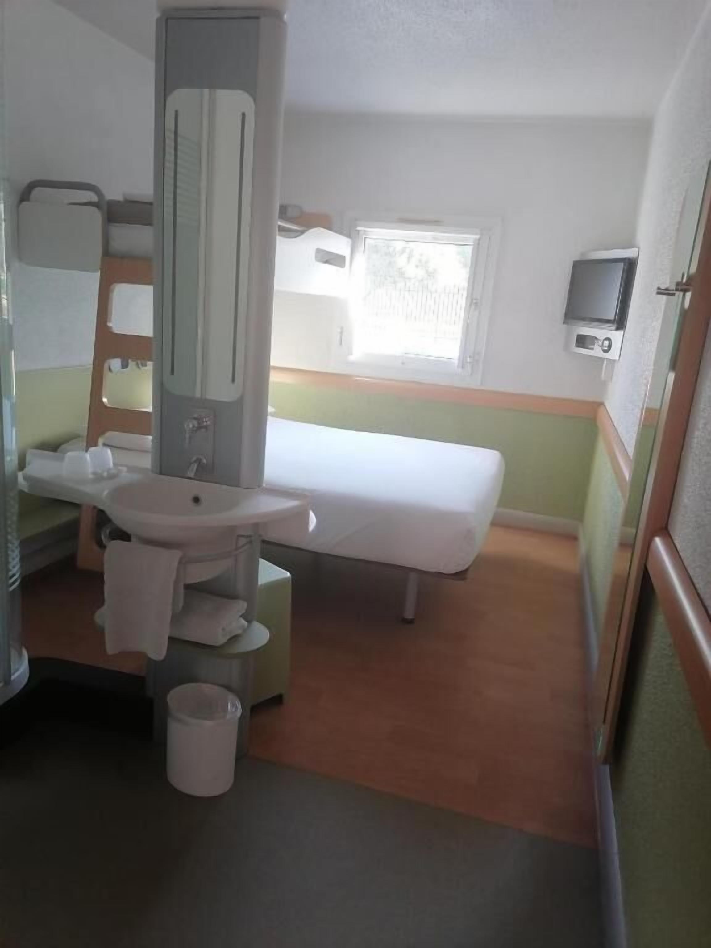 A compact room with a bed, a sink, a mirror, and a television.