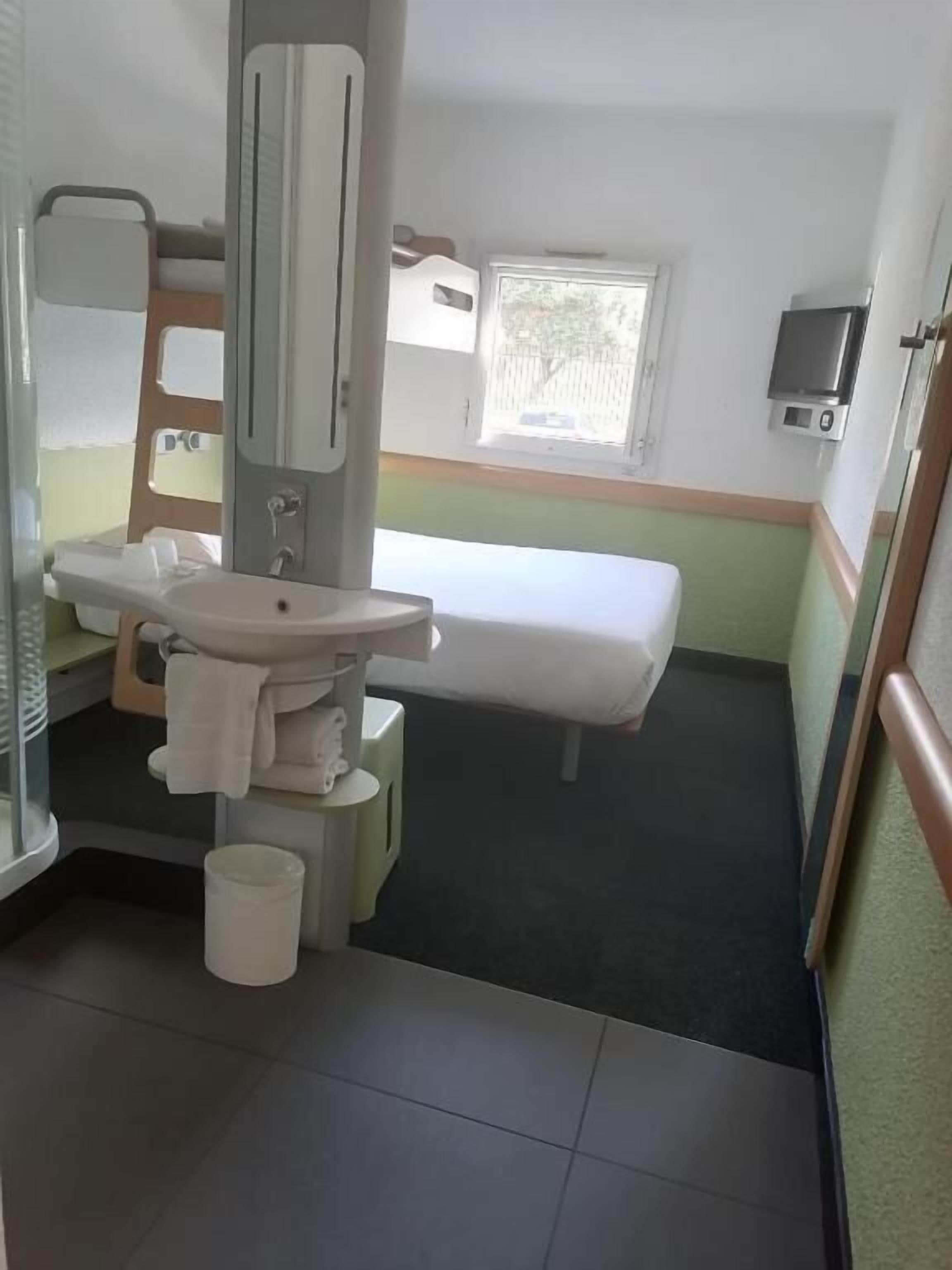 Ein kleines, kompaktes Hotelzimmer mit einem Bett, einem Waschbecken und einem Spiegel.