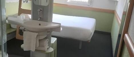 Ein kleines, kompaktes Hotelzimmer mit einem Bett, einem Waschbecken und einem Spiegel.