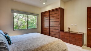 Ein Schlafzimmer mit einem großen Bett, einem Kleiderschrank, einem Schminktisch und einem Fenster mit Blick auf Bäume.