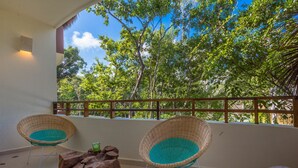 A balcony with two wicker chairs, a wooden log table, and a view of lush green trees. - Peggy 2 BDRM apt sleeps 4 balcony (Tulum)
