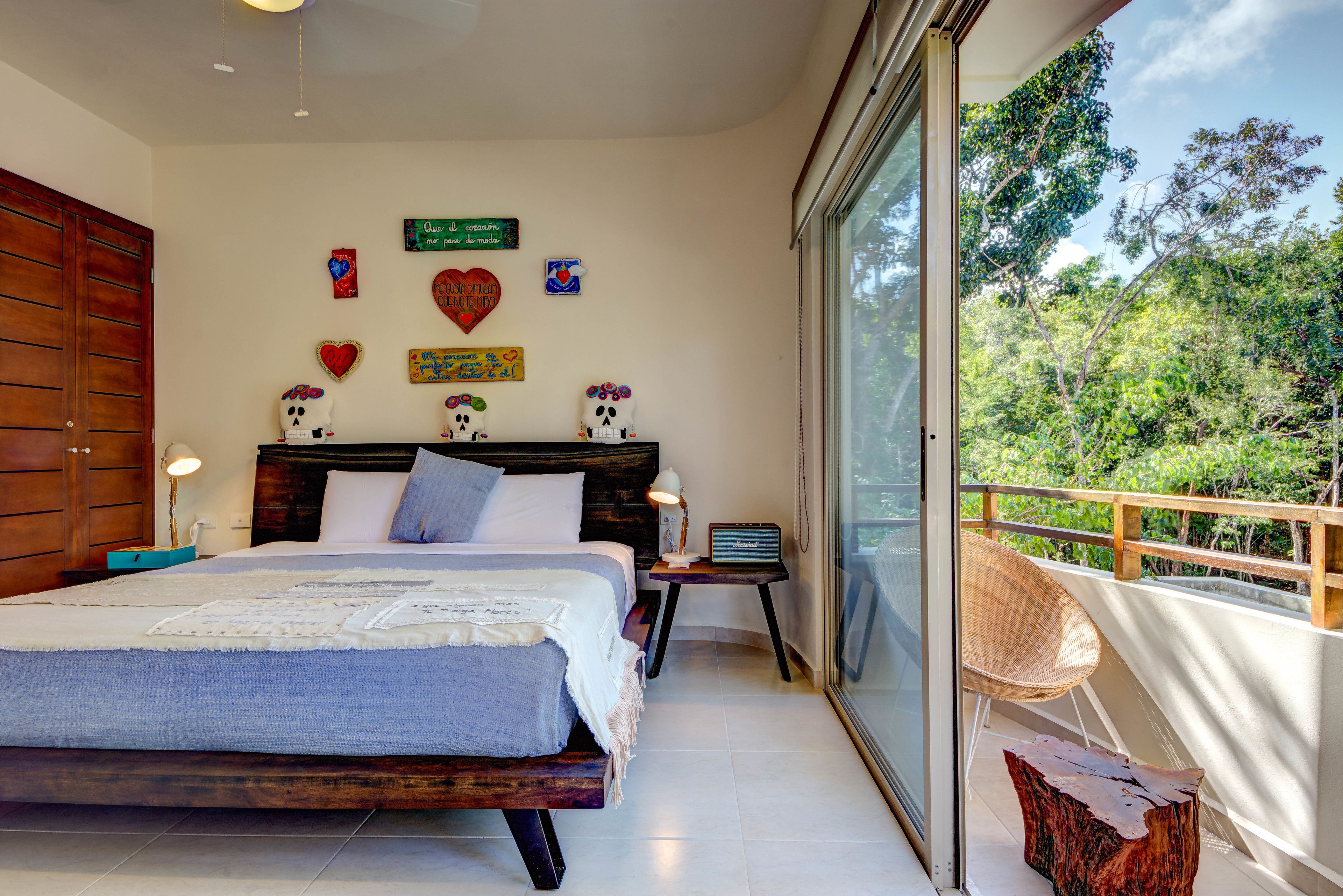 A bedroom with a large bed, a nightstand, a laptop, and a view of trees through a sliding glass door.