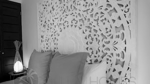 A bedroom with a white, intricately carved headboard, a bedside table with a lamp, and two pillows.