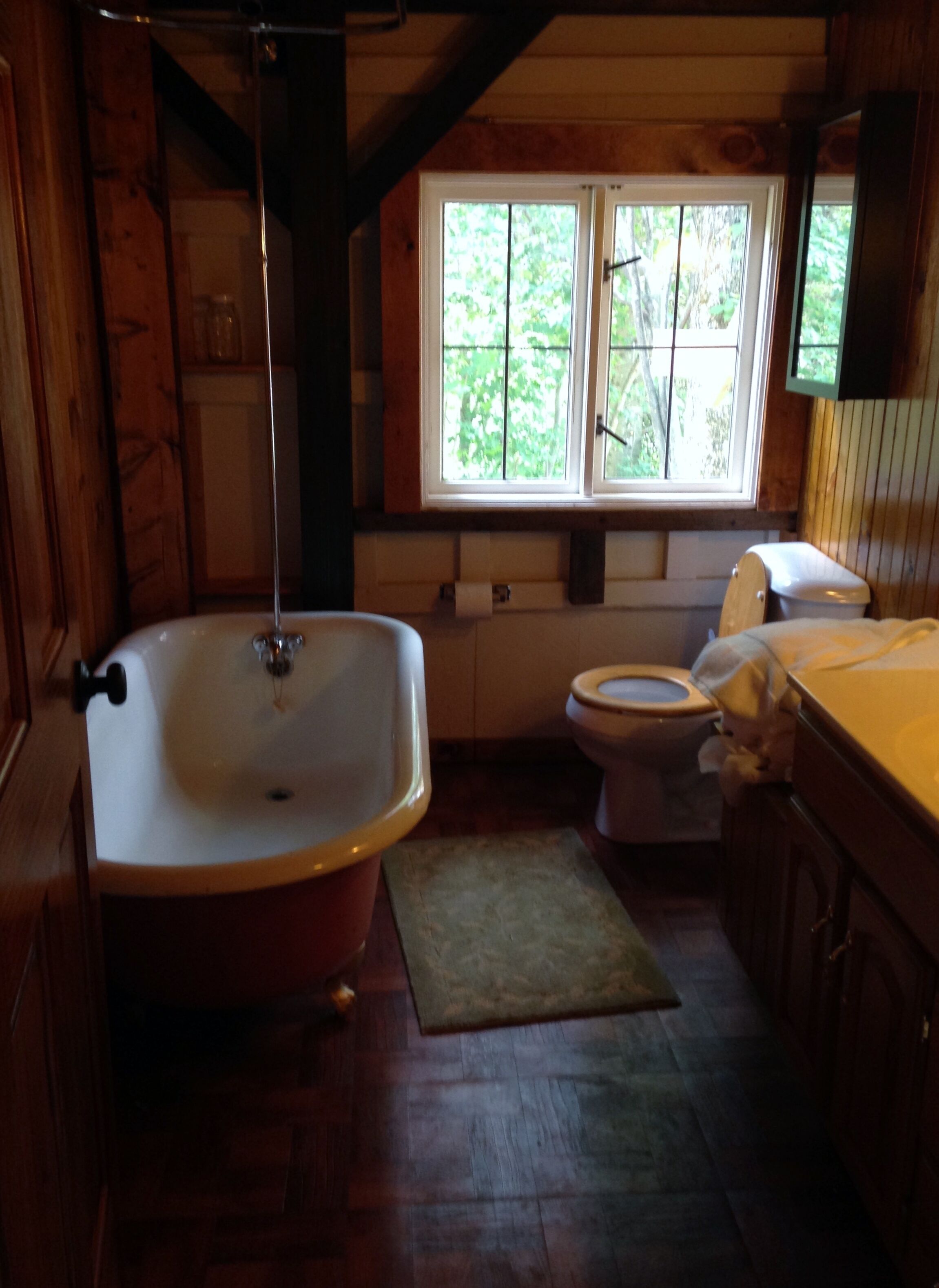 Ein Badezimmer in einer Holzhütte mit Badewanne, Toilette und einem Fenster mit Blick auf Grünflächen.