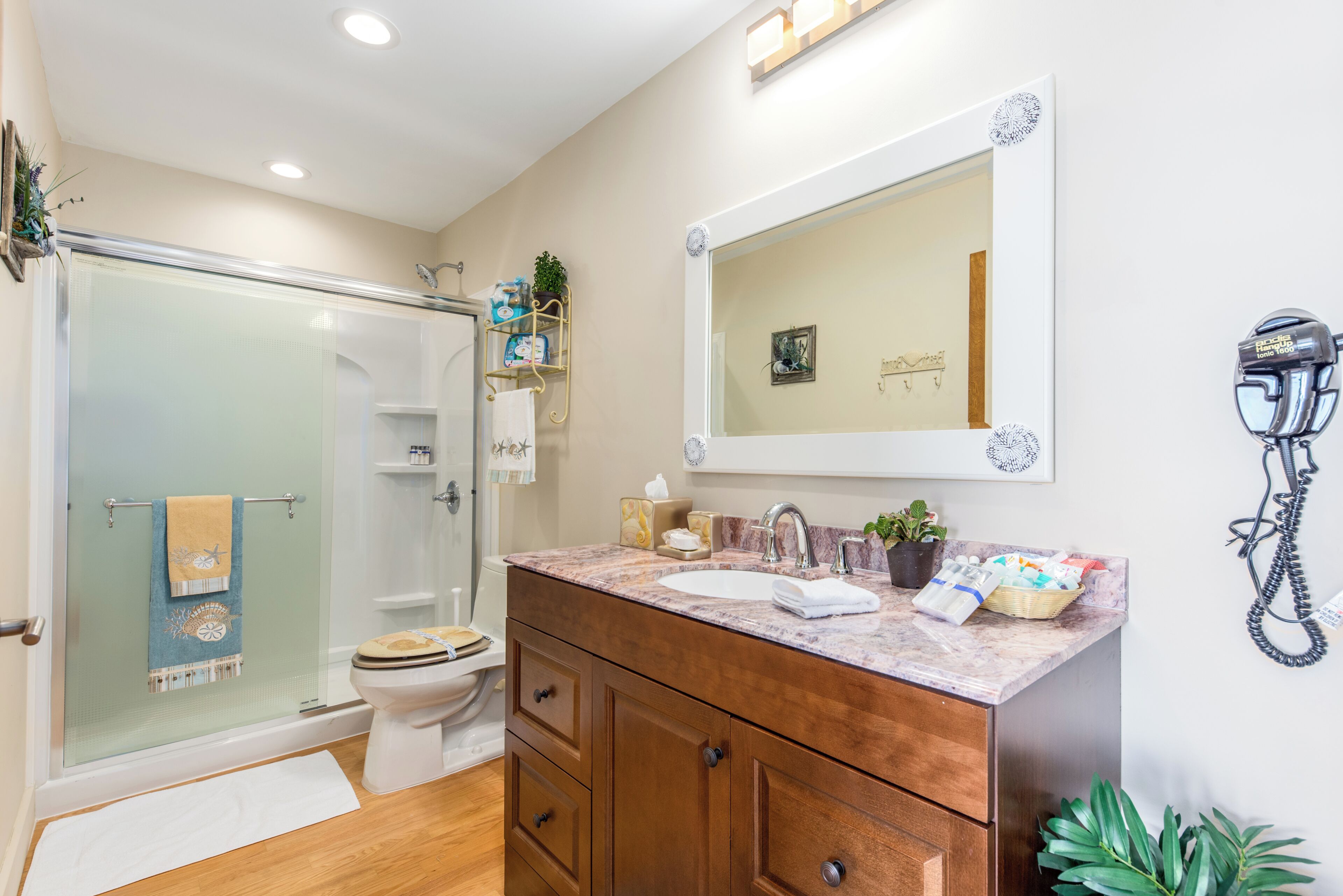 A bathroom with a glass shower enclosure, a white toilet, a wooden vanity with a sink, and a mirror above the vanity.
