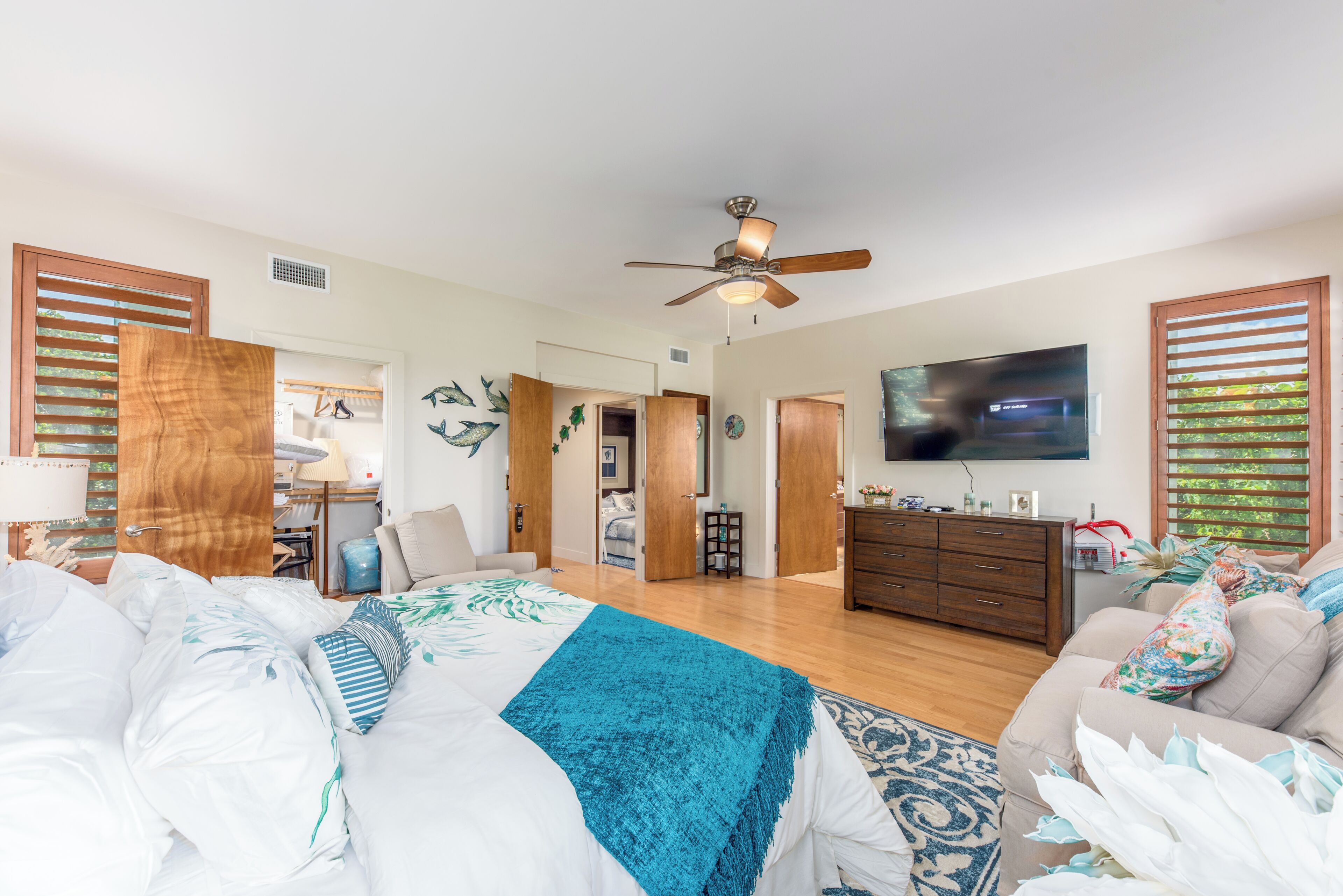 A spacious living room with a large bed, a sofa, a TV, and a ceiling fan.