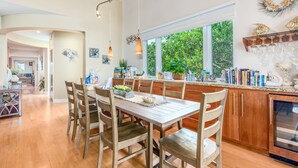 A spacious kitchen with wooden cabinets, a large island with bar tools, and a view of greenery outside.