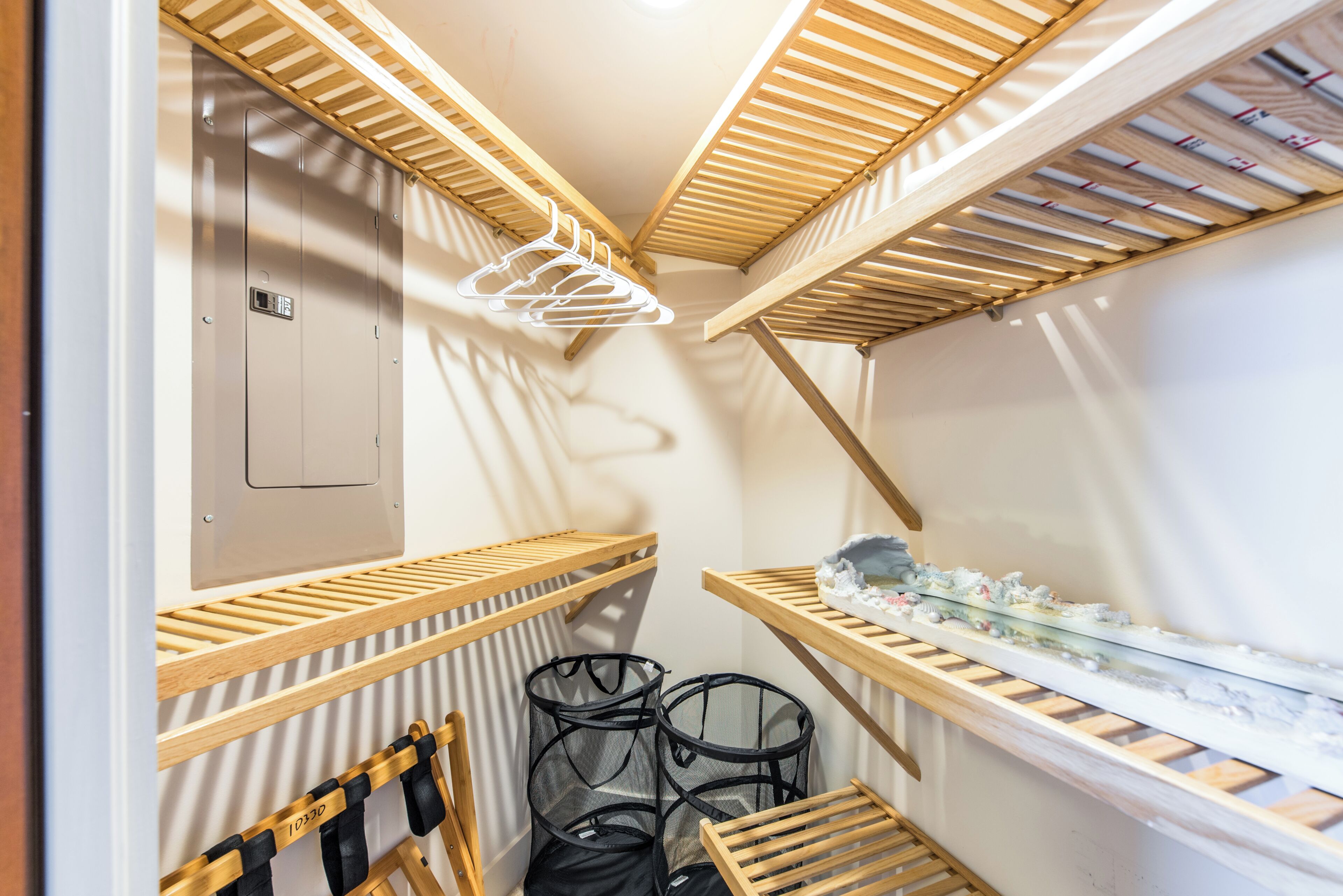 A narrow, enclosed space with wooden slatted shelves for hanging items, a small seating area with a chair, and a wall-mounted storage unit.