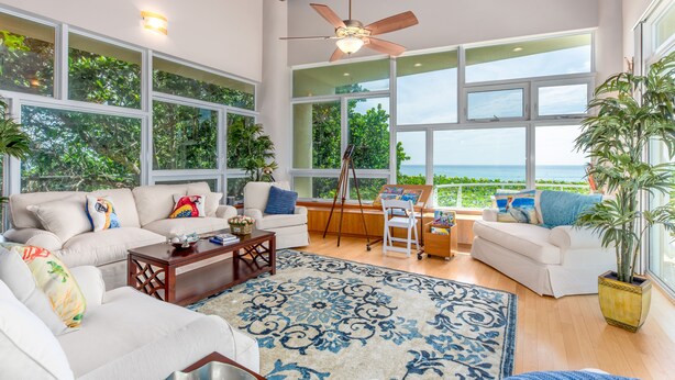 A spacious living room with large windows, a ceiling fan, and a view of the ocean.