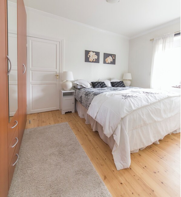 A bedroom with a bed, bedside tables, a nightstand, a door, and two wall-mounted pictures.