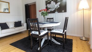Un coin repas avec une table ronde, deux chaises, un vase de fleurs rouges et un tableau accroché au mur.