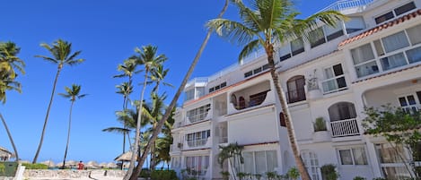 Ein Strandhotel mit mehreren Balkonen, Palmen und blauem Himmel.