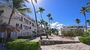 A beachfront hotel with multiple balconies, palm trees, and a sandy beach area. - Beachfront 2BR Apt · Los Corales, Bávaro · Utilities Included (Punta Cana)