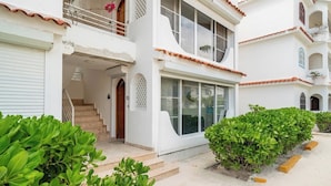 A two-story building with a white exterior, a balcony, and a staircase leading to the entrance. - Beachfront 2BR Apt · Los Corales, Bávaro · Utilities Included (Punta Cana)