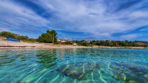 A coastal scene with clear water, a sandy beach, and houses in the background. - Villa Pearl of the Adriatic - discover some undiscoverd(10 meters from sea) (drvenik mali)