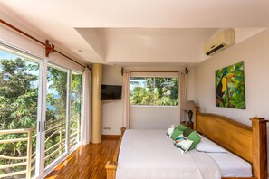 A bedroom with a large window, a bed with pillows, a TV, and a painting on the wall.