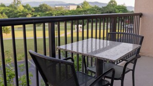 Un balcon avec une table et deux chaises, donnant sur un parc et des bâtiments situés au loin.