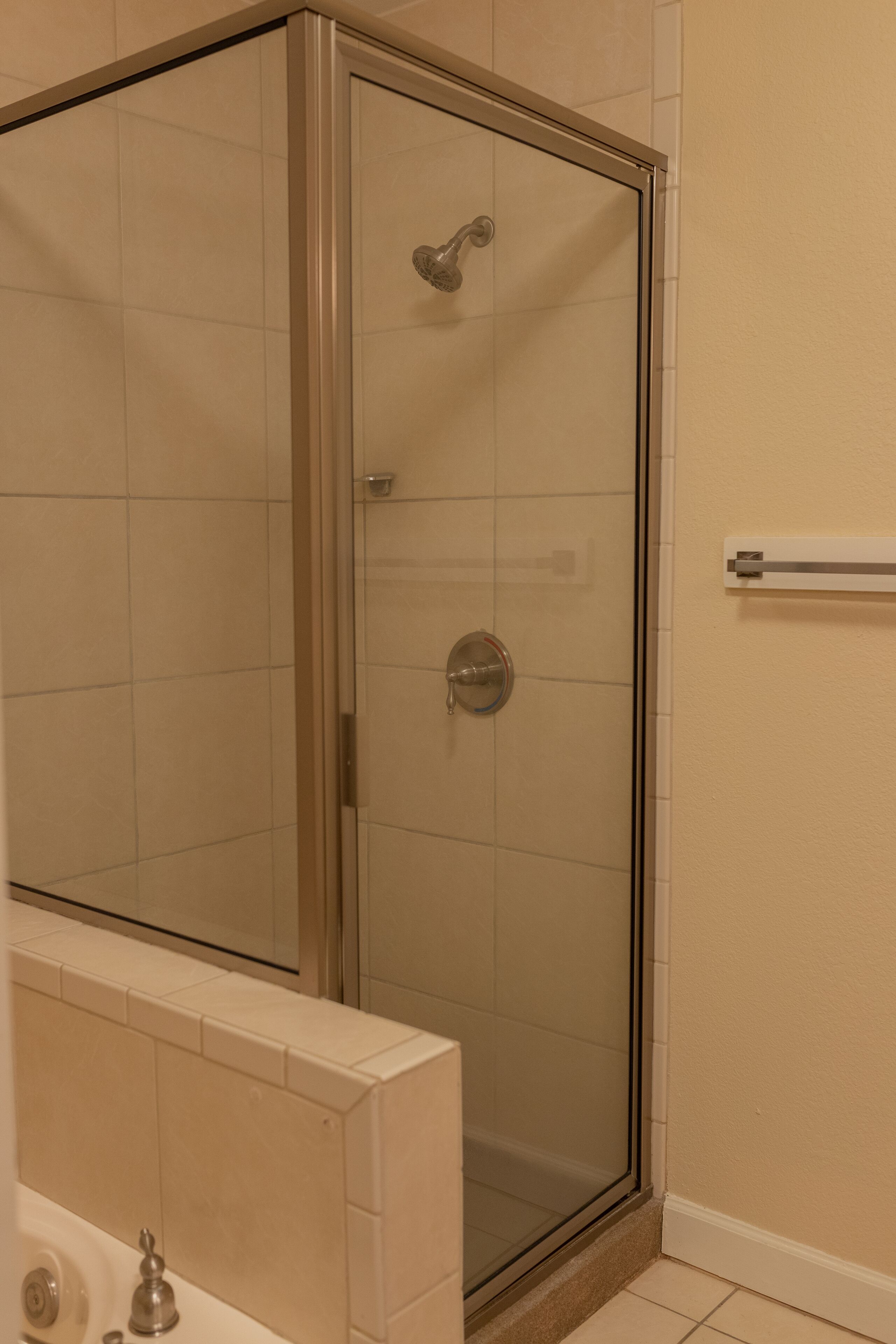 A glass-enclosed shower with a control panel, a towel rack, and a tiled floor.