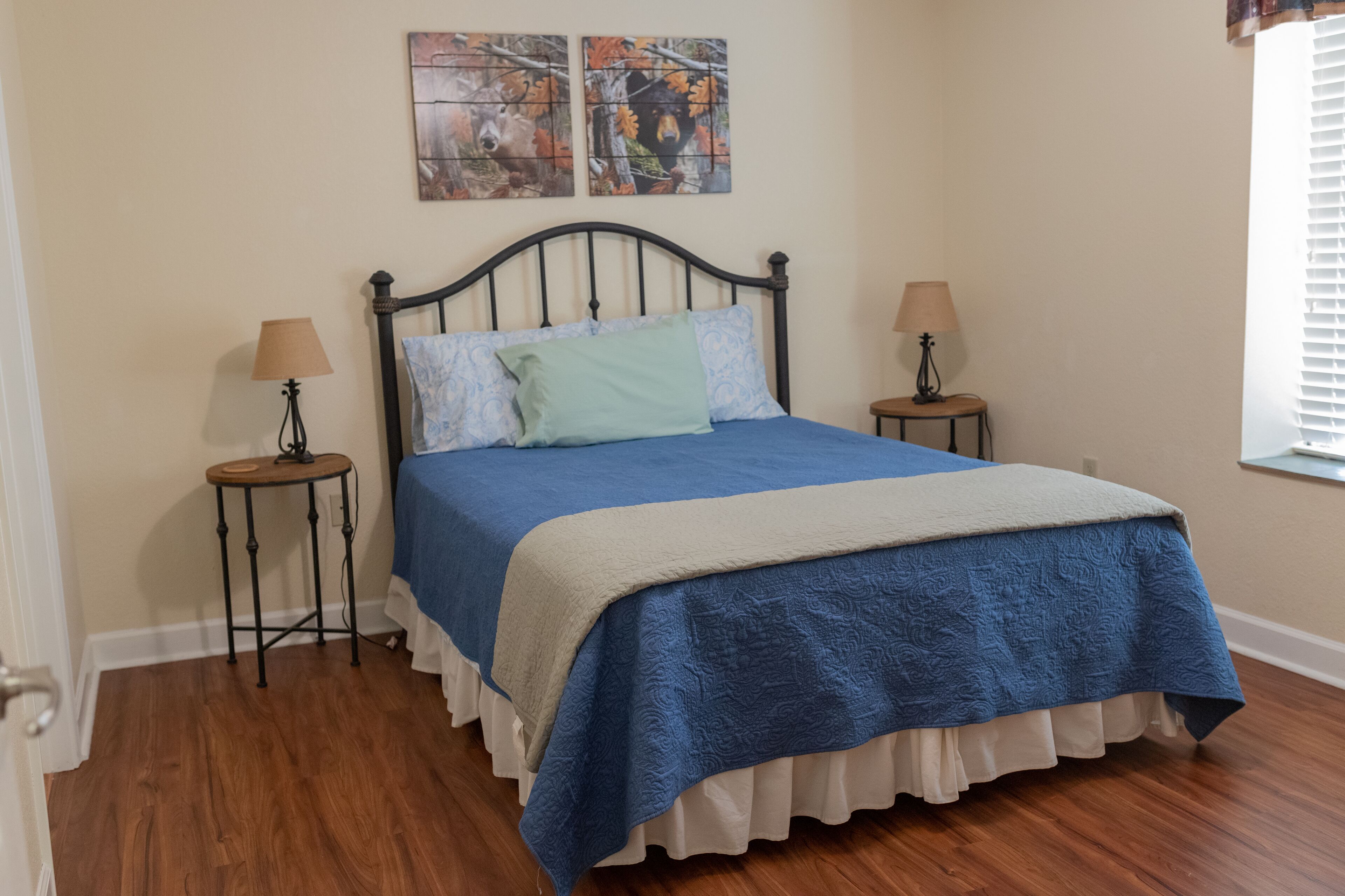 A bedroom with a bed, two bedside tables with lamps, and a window with blinds.