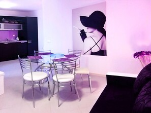 Un coin repas avec une table en verre et des chaises en métal, un coin cuisine équipé d’un four à micro-ondes et de placards, et un mur orné d’une grande œuvre d’art en noir et blanc.