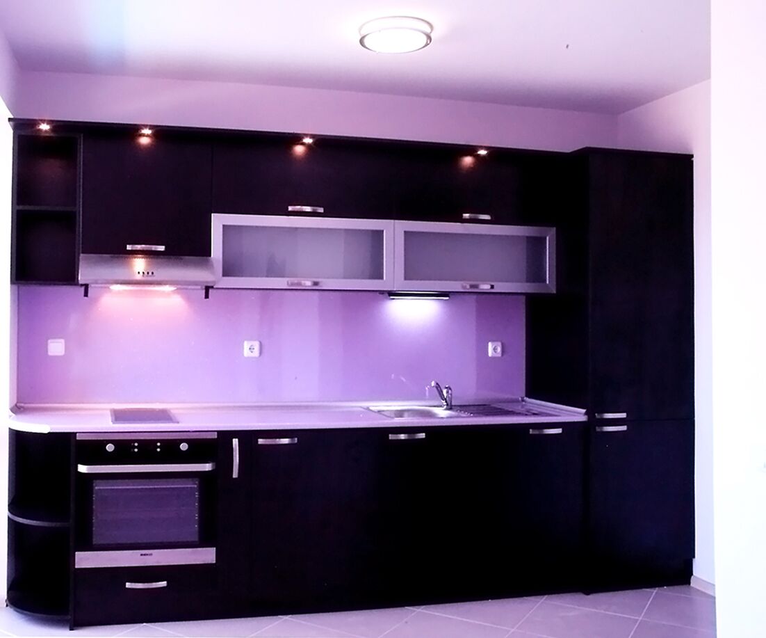 A modern kitchen with dark cabinetry, a stainless steel countertop, a built-in oven, and a double sink.