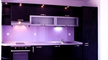A modern kitchen with dark cabinetry, a stainless steel countertop, a built-in oven, and a double sink.