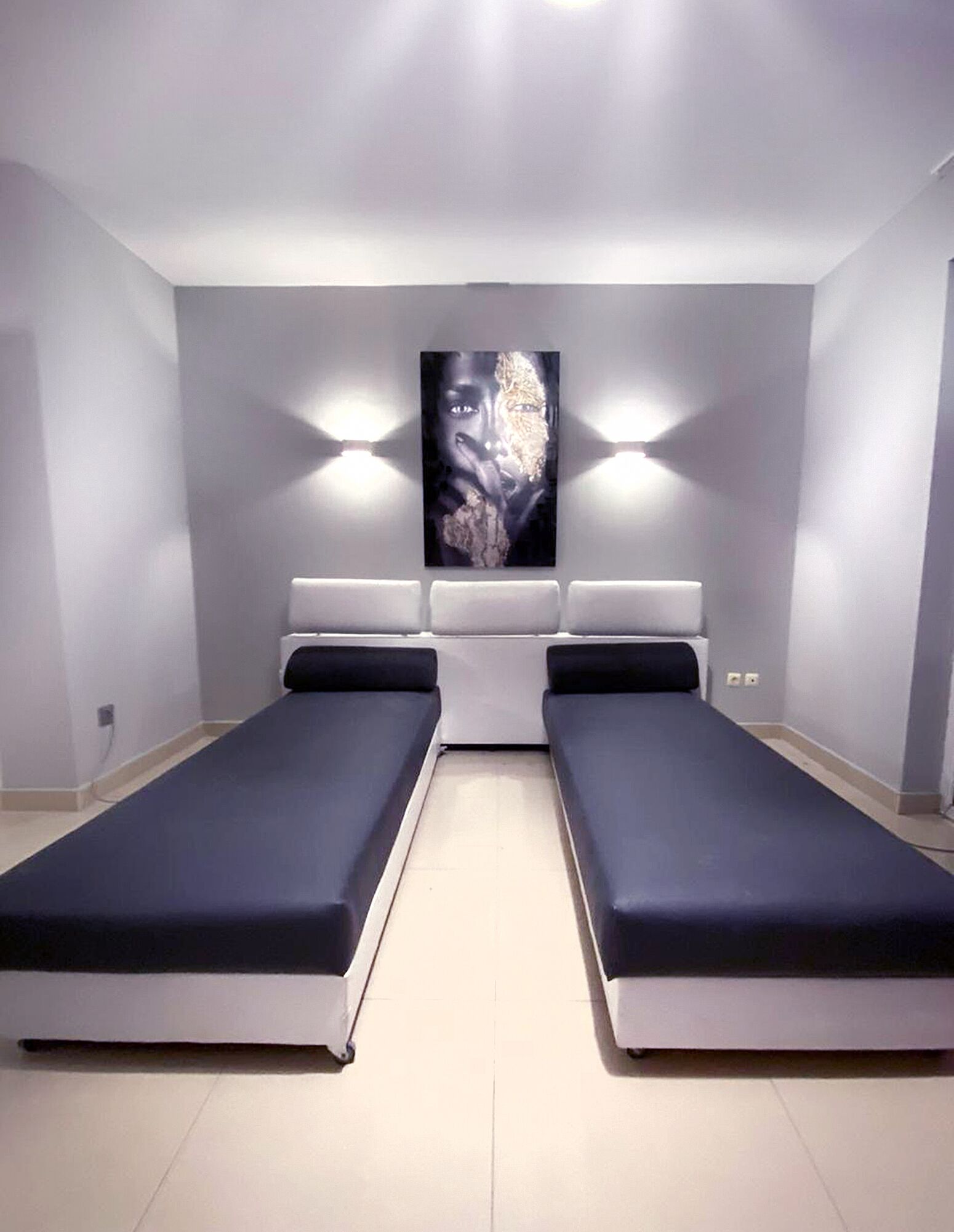 Ein modernes Schlafzimmer mit zwei Einzelbetten, einem großen Wandbild und zwei Wandleuchten.