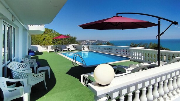 Ein Balkon mit Pool, weißen Stühlen und einem roten Sonnenschirm.