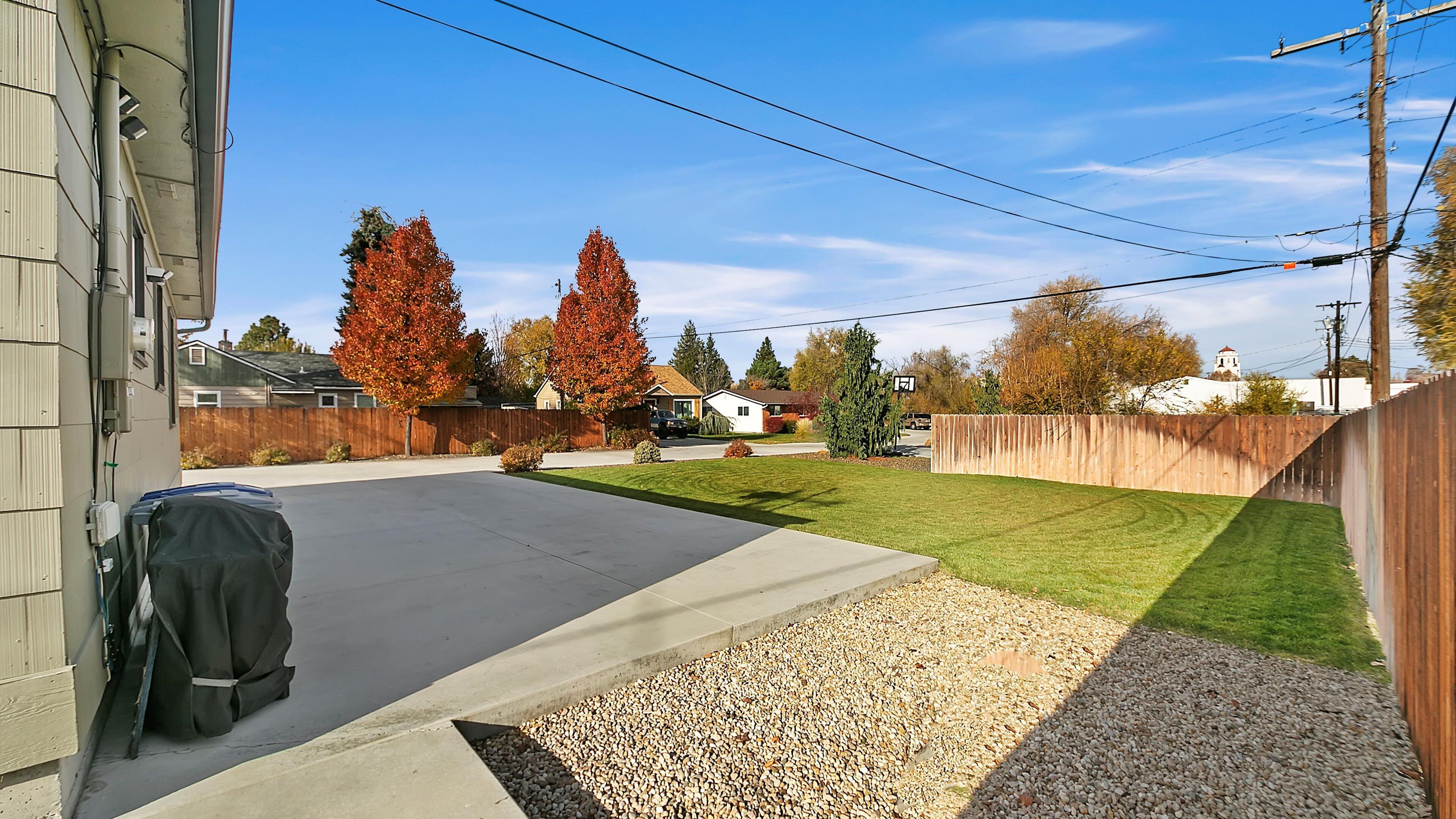 A residential backyard with a concrete patio, a lawn, and a wooden fence.