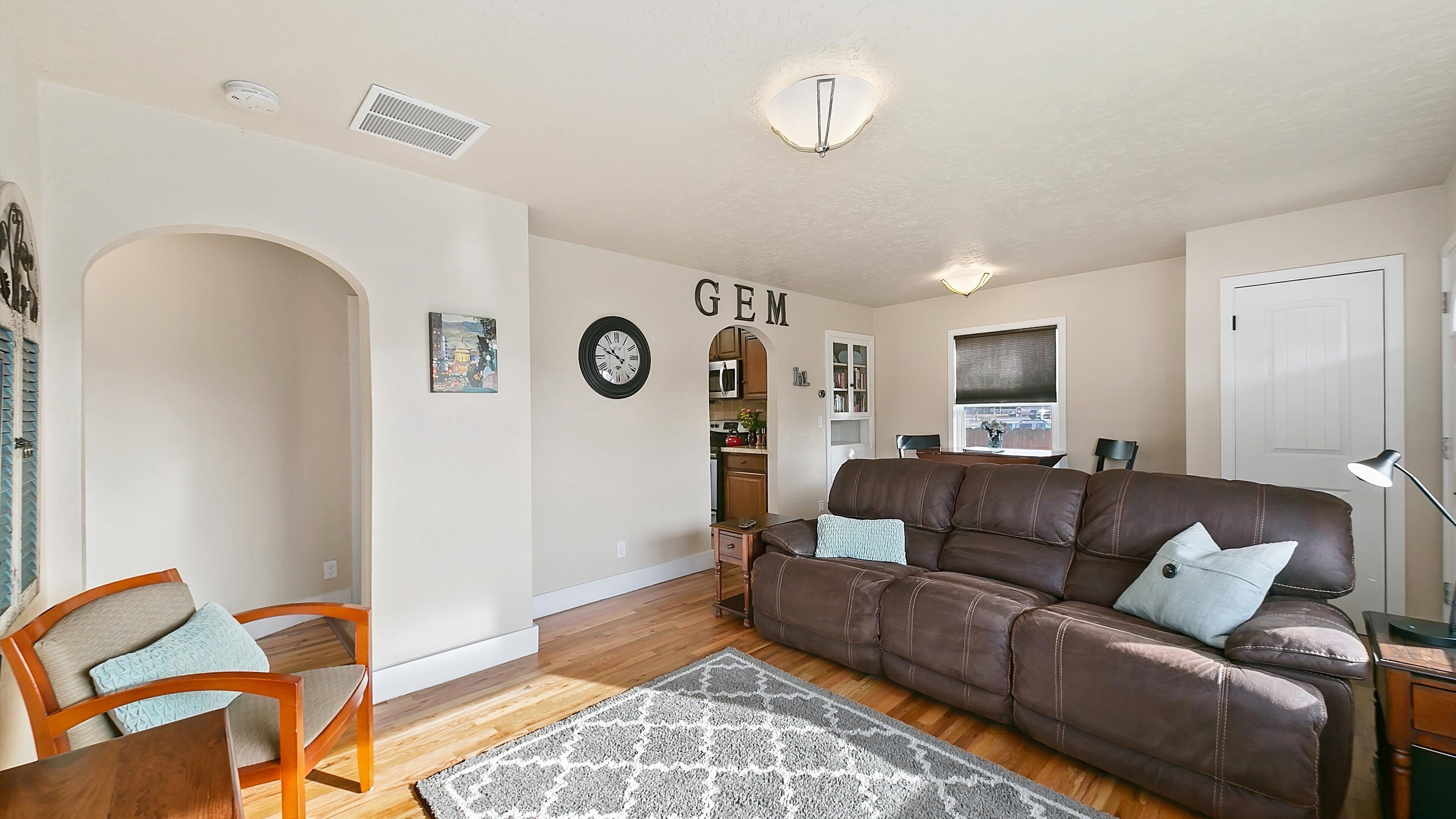 A living room with a brown leather sofa, a wooden coffee table, a patterned rug, and a wall-mounted clock.
