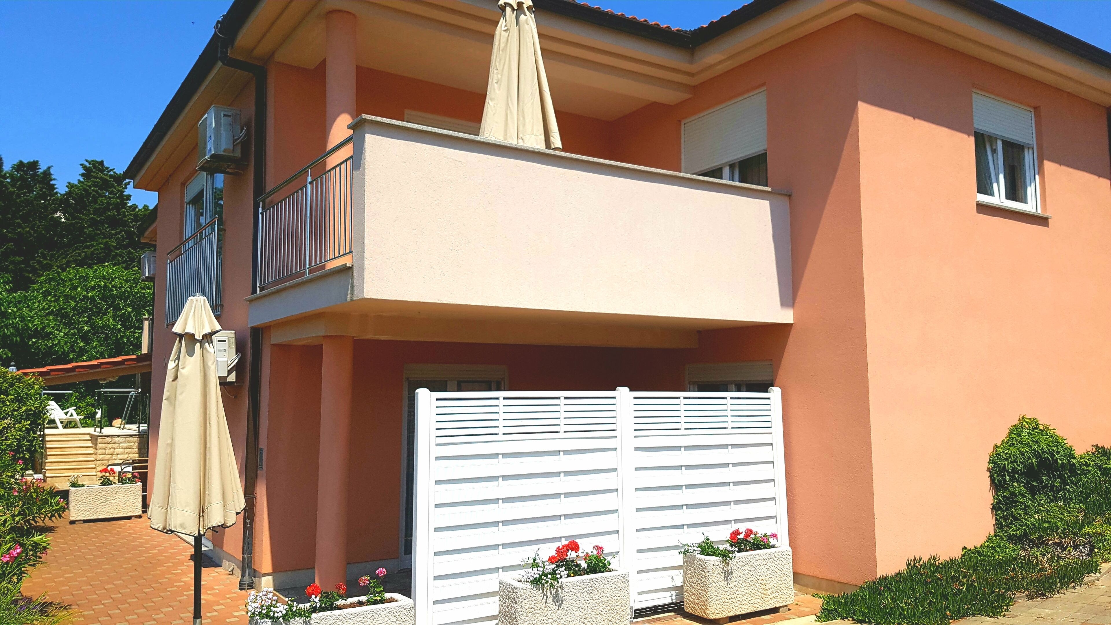 Ein zweistöckiges Gebäude mit Balkon, weißem Tor und Blumenkästen.