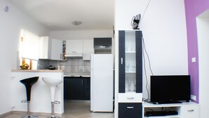 Et moderne køkken med hvide skabe, et sort køleskab og et indbygget TV-møbel med et fladskærms TV.