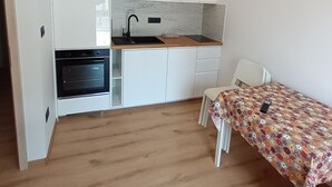 Et kompakt køkken med hvide skabe, en indbygget ovn, en vask og en lille spiseplads med dug med blomster.