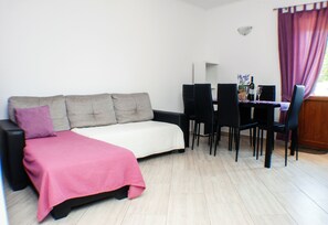 A room with a sofa, a dining table with chairs, a small table with a bottle and glass, and a window with curtains. - Apartment with pool, garden and children's playground (Karojba)