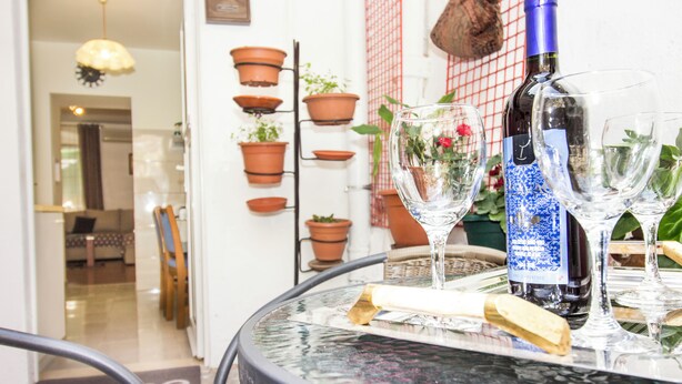 A round glass table with a bottle and glasses, surrounded by terracotta pots and a wicker chair.