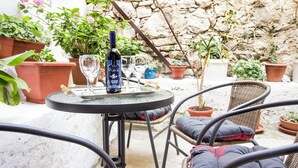 A round table with a bottle of wine, glasses, and a corkscrew. There are wicker chairs with cushions around the table.
