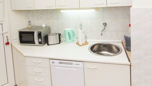 A compact kitchen with white cabinets, a microwave, toaster, kettle, and a dishwasher.