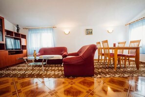 A living room with a sofa, armchair, glass coffee table, and a dining table with chairs.
