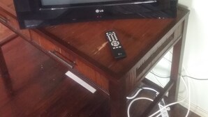 A flat-screen TV on a wooden stand with a remote control beside it. - Aanola Villas 6B Quiet boulevard (Charlotte)