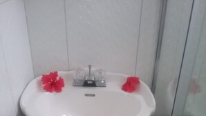 A white pedestal sink with two faucets and a drain, flanked by white tiles. - Aanola Villas 6B Quiet boulevard (Charlotte)