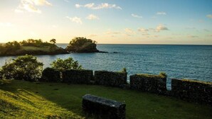 A coastal landscape with a grassy area, stone walls, and a body of water. - Aanola Villas 6B Quiet boulevard (Charlotte)