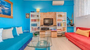 Un salon avec un mur bleu, un canapé rouge, un divan bleu et une table basse en verre.
