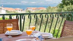 Une table avec deux verres de jus d’orange et une assiette, sur un balcon donnant sur un paysage magnifique avec la mer et des bâtiments.