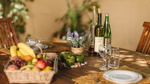 Ein Holztisch ist gedeckt mit einer Obstschale, Weinflaschen, Gläsern und einem Blumentopf.
