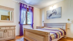 Ein Schlafzimmer mit einem hölzernen Bett, einem Nachttisch, einer Kommode und einem Fenster mit violetten Vorhängen.