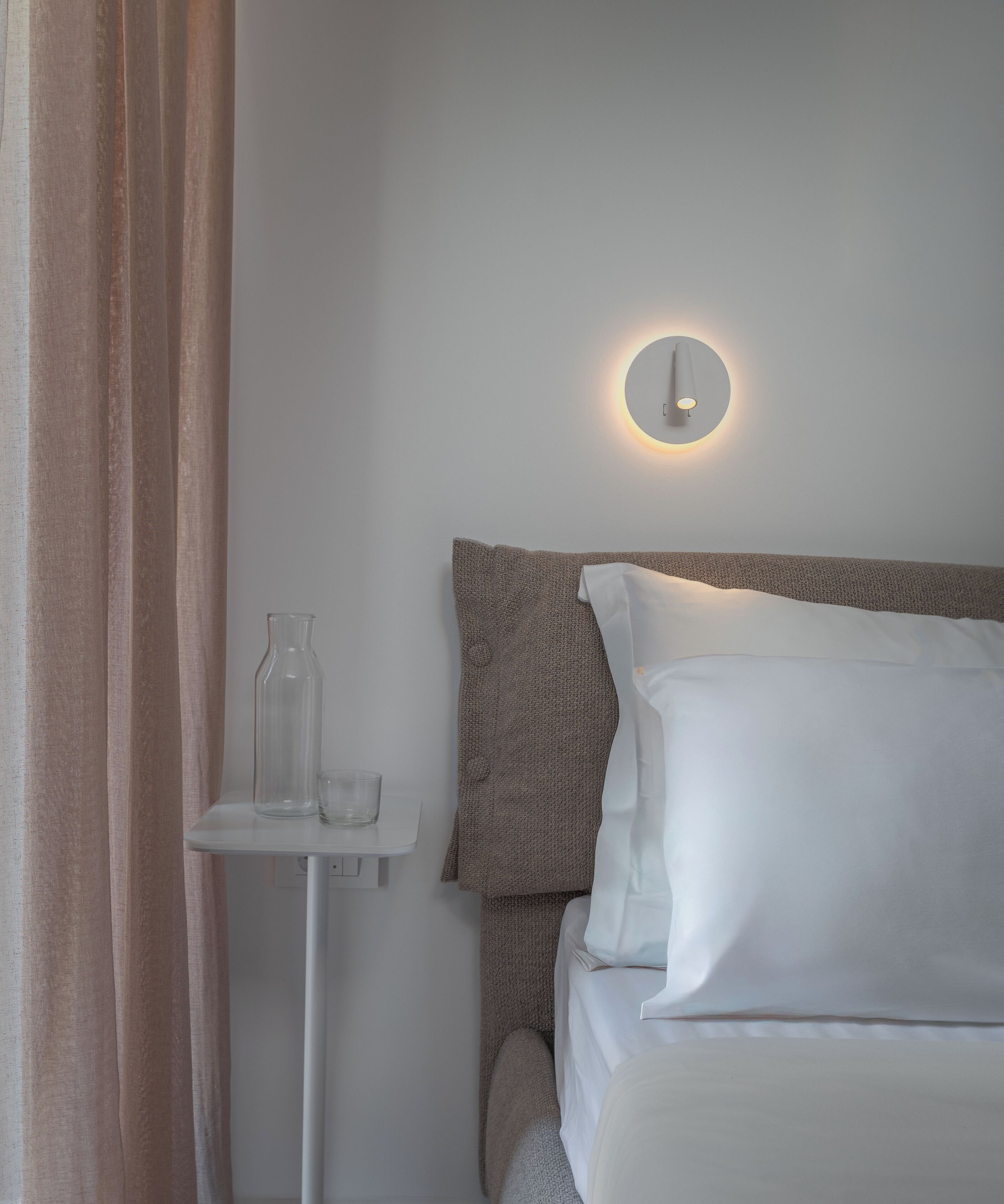 Una camera da letto con un letto, un comodino con un bicchiere e una lampada a parete.
