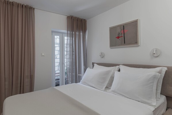A hotel room with a bed, white curtains, a door, and a wall-mounted artwork.