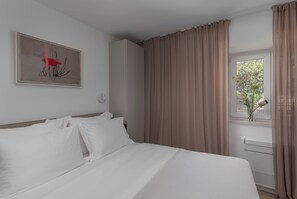 Une chambre d’hôtel avec un lit, une fenêtre avec des rideaux, un radiateur et un tableau au mur.