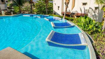 A swimming pool with clear blue water, surrounded by lush greenery and palm trees.